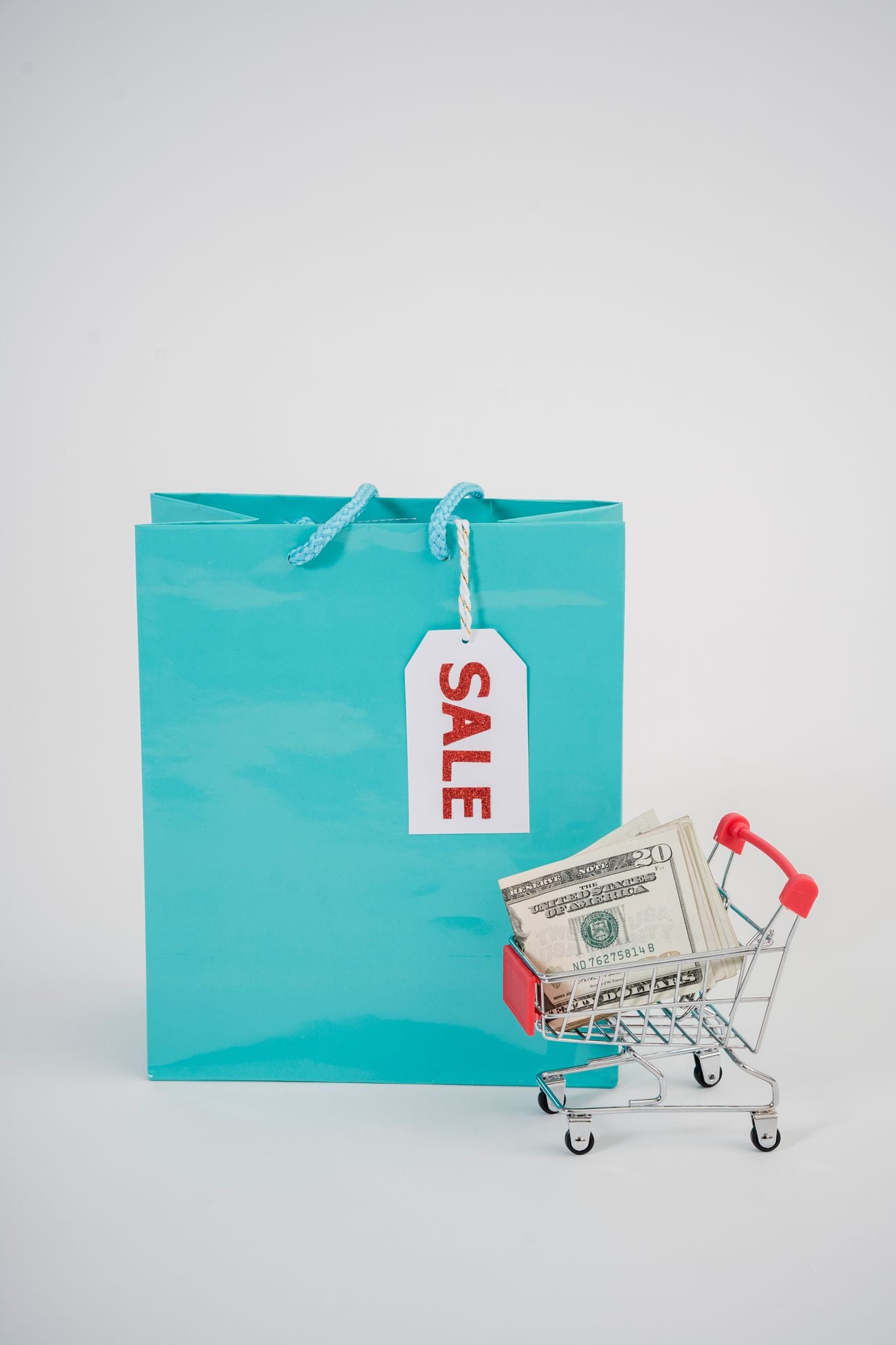 Image of a miniature shopping cart with money and a blue shopping bag labeled sale.